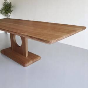 Table de séjour en chêne massif, fabriquée à la main avec un pied circulaire unique, design moderne et bords arrondis, idéale pour un intérieur élégant et contemporain.
