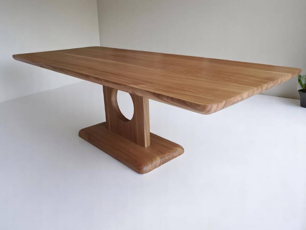 Table de séjour en chêne massif, fabriquée à la main avec un pied circulaire unique, design moderne et bords arrondis, idéale pour un intérieur élégant et contemporain.