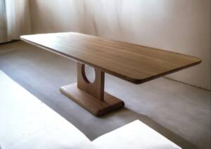 Table de séjour en chêne massif, fabriquée à la main avec un pied circulaire unique, design moderne et bords arrondis, idéale pour un intérieur élégant et contemporain.