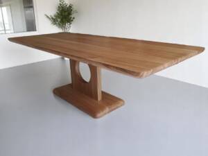 Table de séjour en chêne massif, fabriquée à la main avec un pied circulaire unique, design moderne et bords arrondis, idéale pour un intérieur élégant et contemporain.